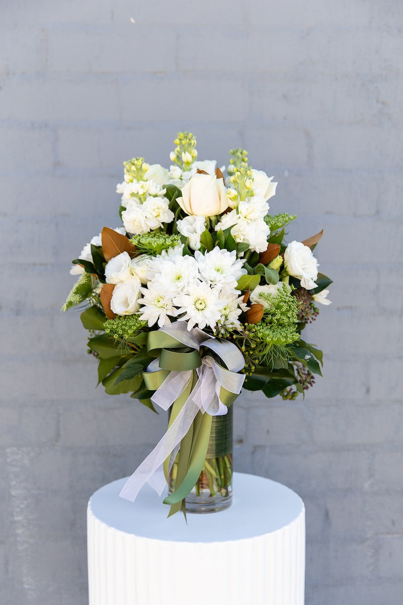 The Alaska floral arrangement - an elegant, designer bouquet featuring a combination of cream and white blooms and lush foliage, presented in a glass cylinder vase. Approximate height is 40cm.