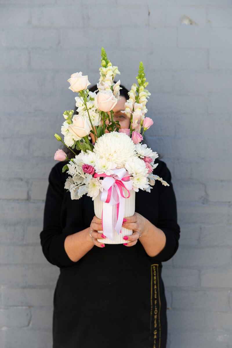 A Donvale Flower Gallery team member holding Ella - a floral arrangement of seasonal pastel blooms in a ceramic pot.