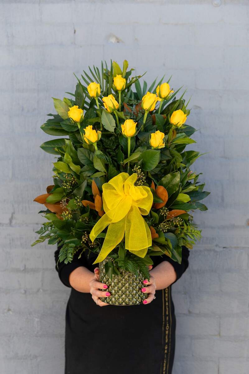 Photo of a Donvale Flower Gallery team member holding the Ingrid rose floral arrangement consisting of 10x long-stemmed yellow roses with lush greenery.