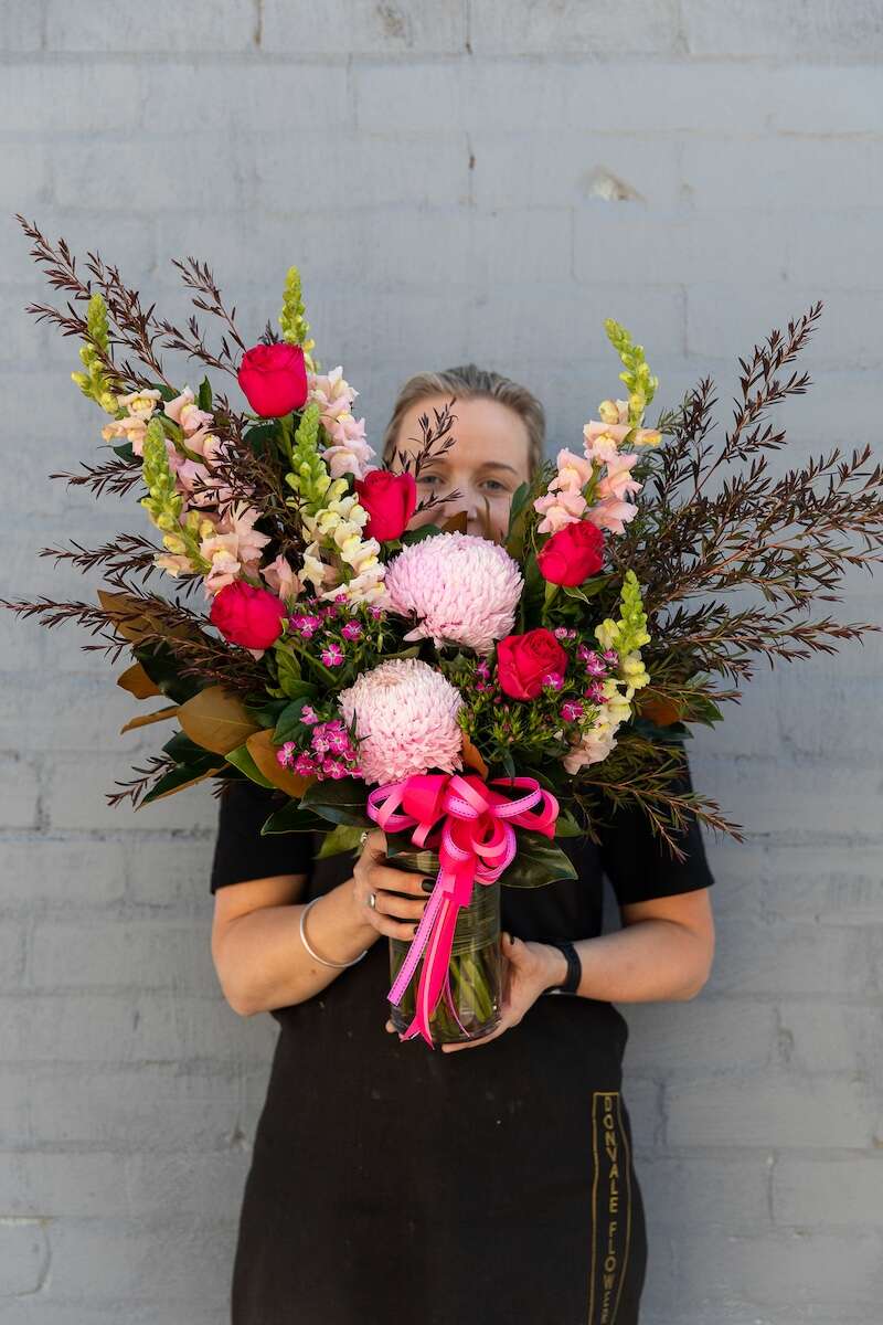 Image of a Donvale Flower Gallery team member holding Elizabeth: a modern pink-toned bouquet presented in a glass vase, adorned with a luxurious matching bow. 