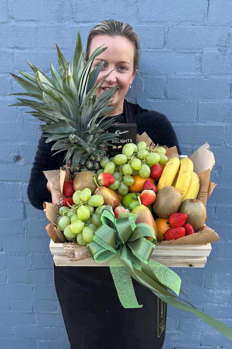 Image of a Donvale Flower Gallery team member holding the Tasteful gift hamper consisting of an assortnment of fresh fruit and chocolate.