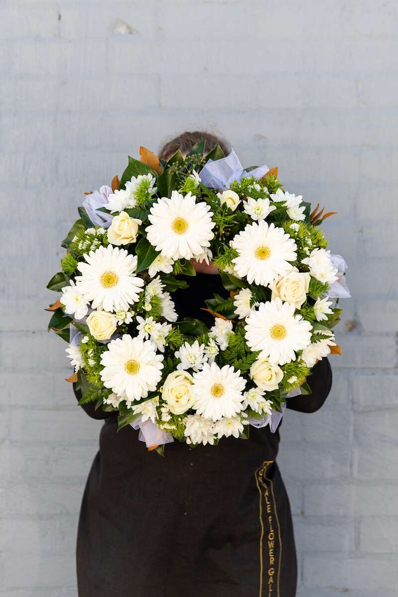 Image of a Donvale Flower Gallery team member holding the white & green wreath available to purchase.